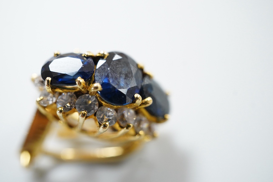A pair of sapphire earrings, each set with three oval sapphires, within a border of brilliant-cut cubic zirconias, mounted in gold, length 1.4cm each, clip and retractable post fittings
